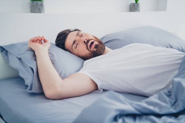 Persona durmiendo con expresión de malestar, representando la relación entre apnea del sueño y dolor de cabeza matutino